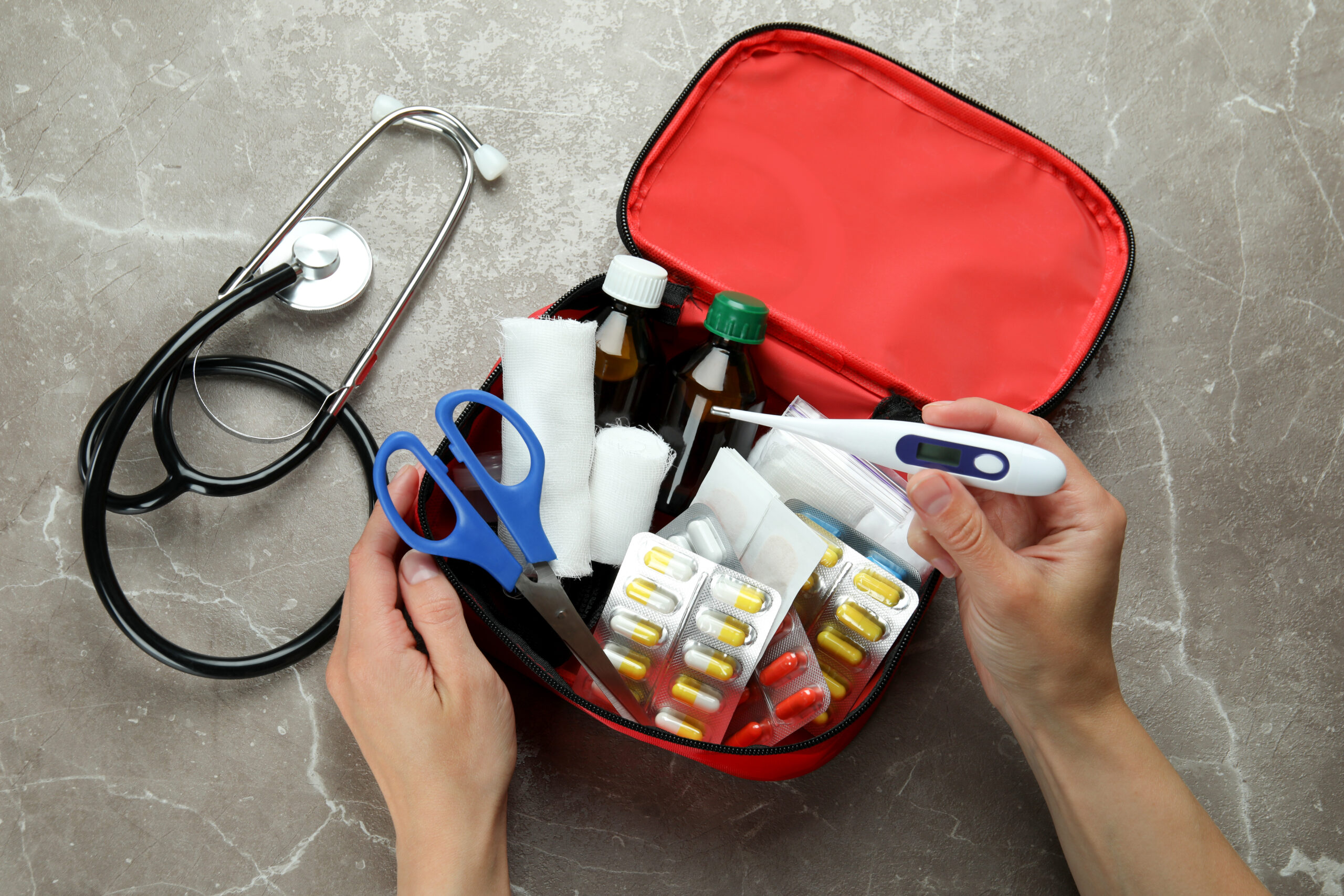 womans hands in a first aid kit holding a thermometer